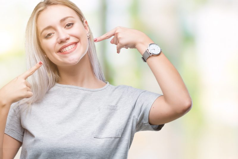 Young blonde woman over isolated background smiling confident showing and pointing with fingers teeth and mouth. Health concept.